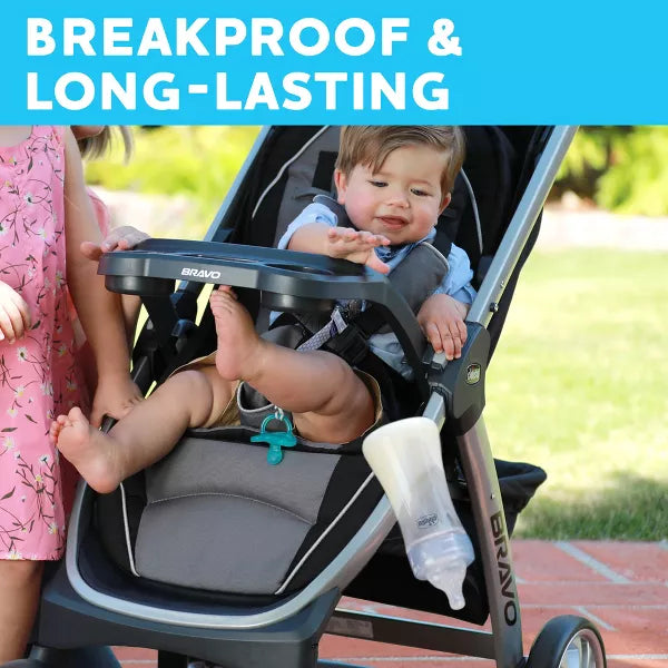 Child in a stroller with a tray attached, outdoors on a sunny day.