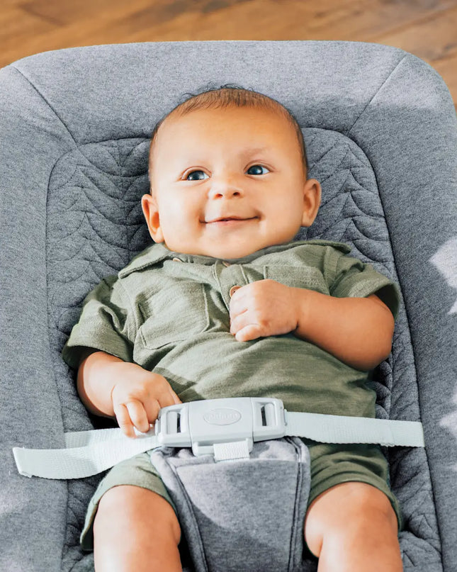 Baby in a gray baby seat with a wooden floor background