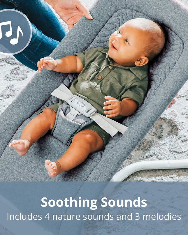 Baby lying in a gray baby bouncer with soothing sounds feature.