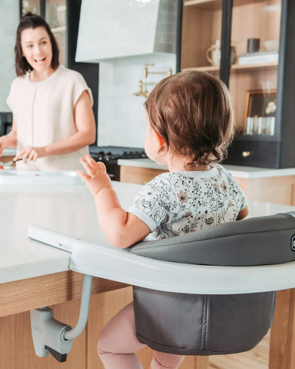 Child in a high chair at a kitchen counter with a woman in the background