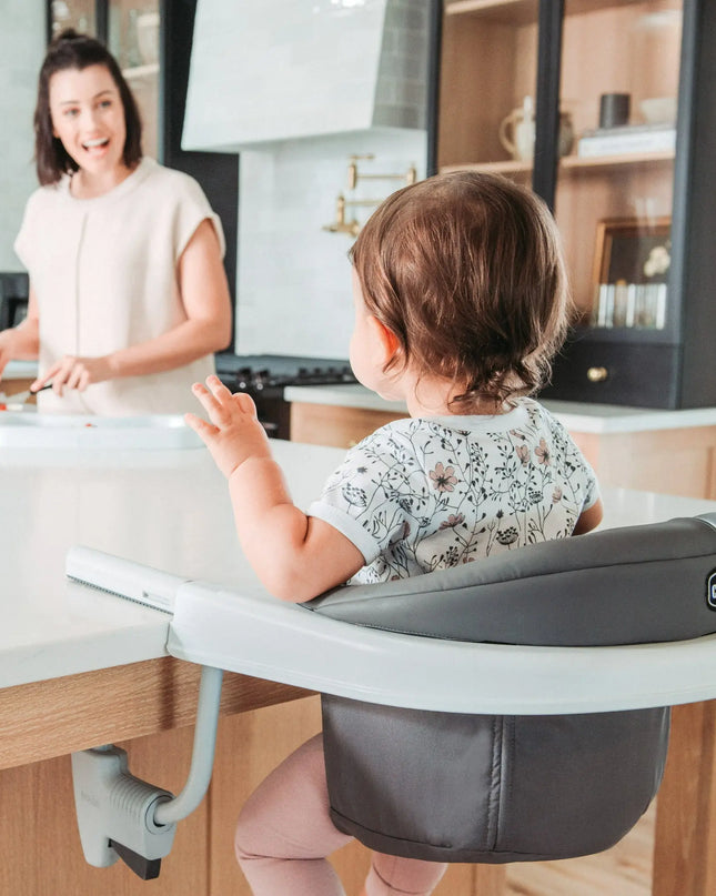 Child in a high chair at a kitchen counter with a woman in the background