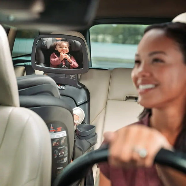 Woman driving a car with a child in a rear-facing car seat and a mirror showing the child.