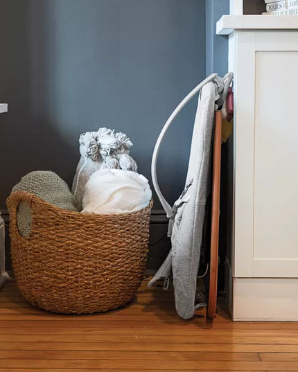 Woven basket with folded clothes on a wooden floor next to a white cabinet.