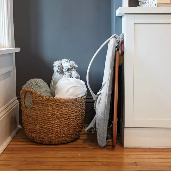 Woven basket with folded clothes on a wooden floor next to a white cabinet.
