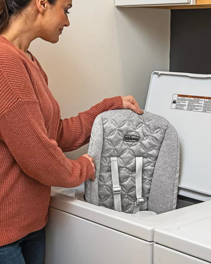 Person placing a gray quilted backpack into a washing machine.