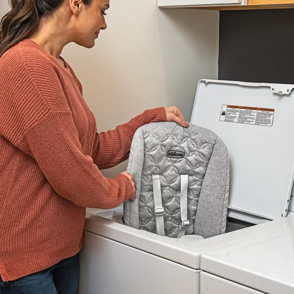 Person placing a gray quilted backpack into a washing machine.