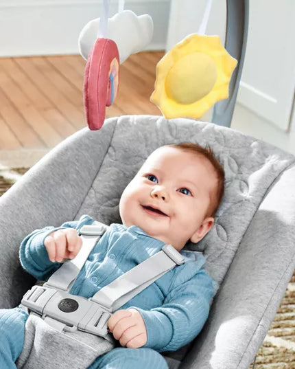 Baby in a gray baby bouncer with toys hanging above, smiling.