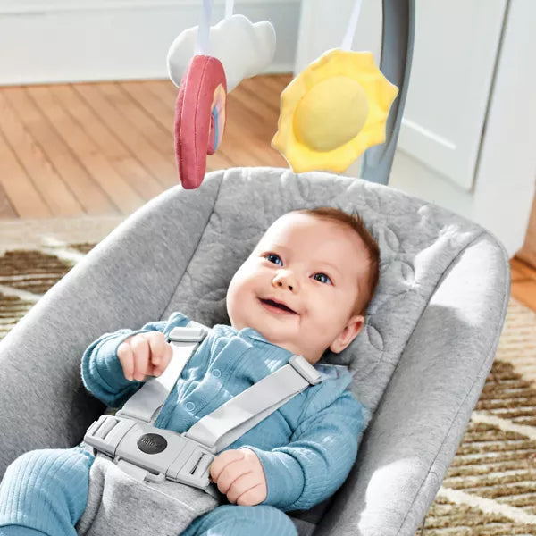 Baby in a gray baby bouncer with toys hanging above, smiling.