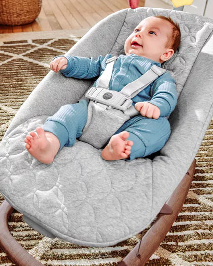 Baby in a gray baby bouncer on a carpeted floor