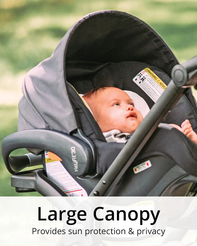Baby in a car seat with a large canopy, providing sun protection and privacy, outdoors.