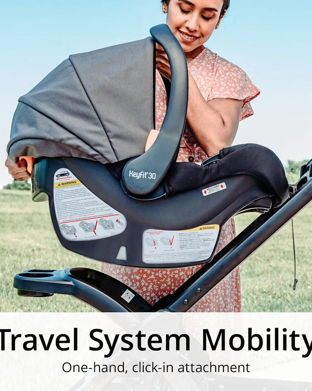 Woman holding a baby car seat with 'Maxi-Cosi' branding outdoors.