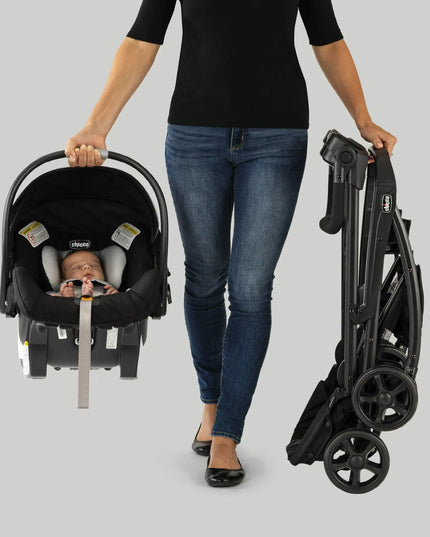 Woman holding a folded stroller and a car seat with a baby inside on a gray background