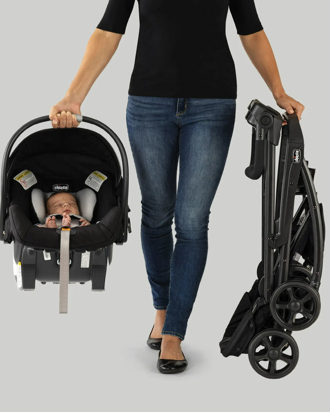 Woman holding a folded stroller and a car seat with a baby inside on a gray background