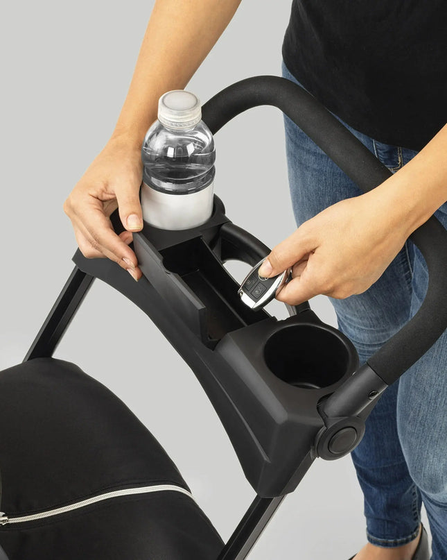 Person using a stroller cup holder with a water bottle and phone.
