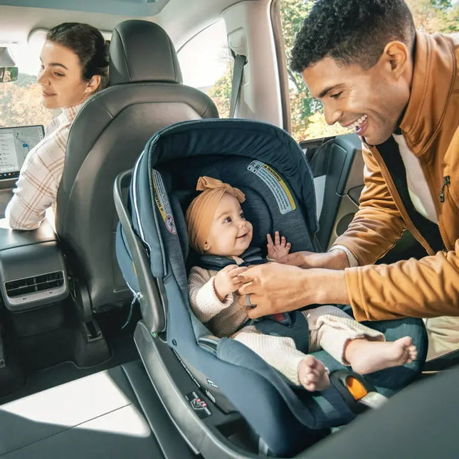 Family in a car with a baby in a car seat, smiling and interacting.