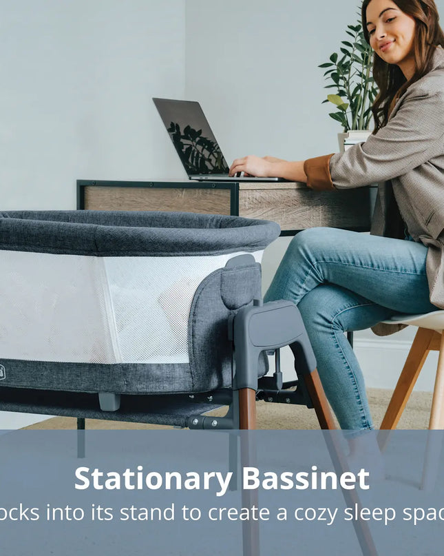 Woman using a laptop with a stationary bassinet in the foreground