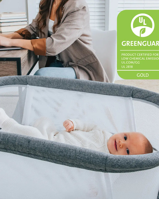 Baby in a crib with a woman working at a desk, featuring a Greenguard Gold certification logo.