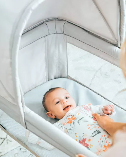 Baby in a swaddle blanket lying in a bassinet with a woman holding the bassinet.