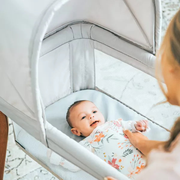 Baby in a swaddle blanket lying in a bassinet with a woman holding the bassinet.