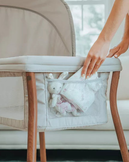 Person reaching into a mesh pocket attached to a crib with baby toys inside.