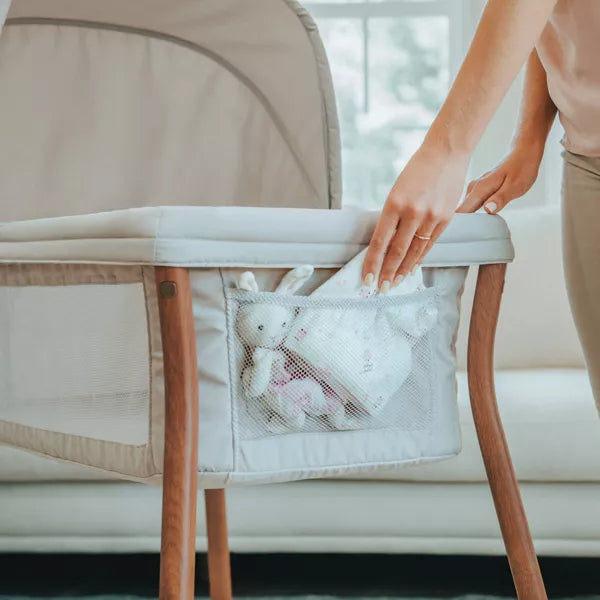 Person reaching into a mesh pocket attached to a crib with baby toys inside.