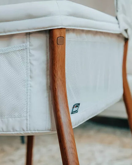 Close-up of a baby crib with wooden legs and white mattress