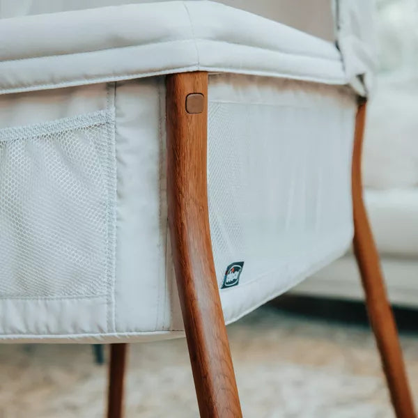 Close-up of a baby crib with wooden legs and white mattress