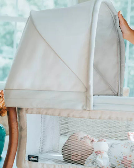 Baby in a crib with a beige canopy, surrounded by a blurred indoor setting.