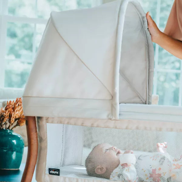 Baby in a crib with a beige canopy, surrounded by a blurred indoor setting.