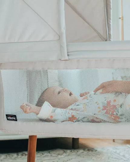 Baby in a crib with a mesh side panel, showing a brand logo.