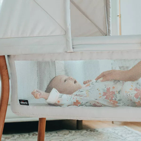 Baby in a crib with a mesh side panel, showing a brand logo.