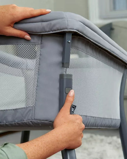 Person adjusting a gray crib with a hand on the handle and another hand on the top corner.