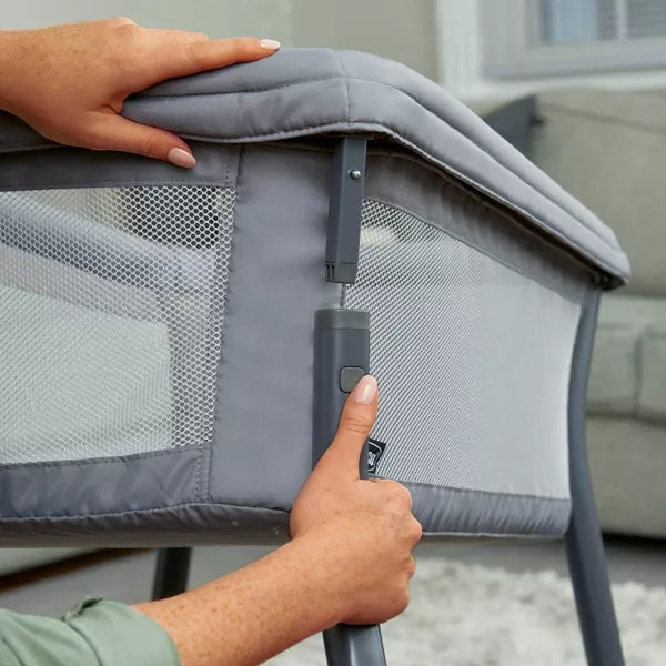 Person adjusting a gray crib with a hand on the handle and another hand on the top corner.