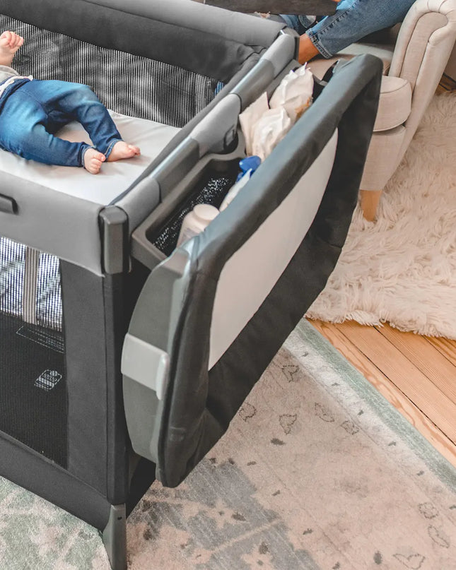 Child in a playpen with a person adjusting the gate in a home setting