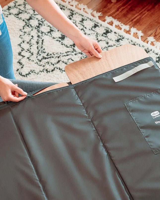 Person opening a large gray bag on a wooden floor with a rug.
