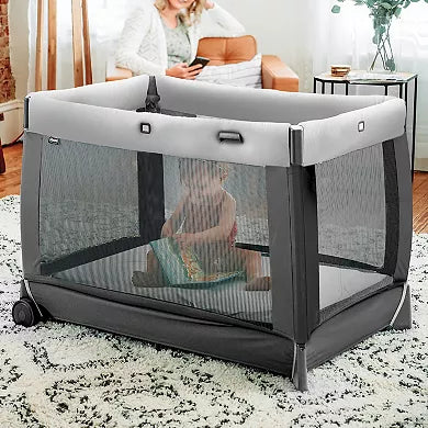Portable crib on a rug with a person sitting inside, in a home setting.