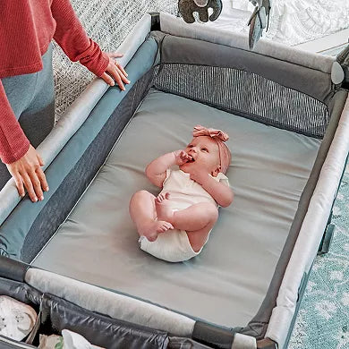 Baby in a portable crib with a person adjusting the sides