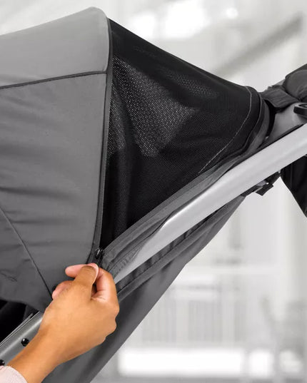 Hand adjusting a gray stroller canopy with a blurred background