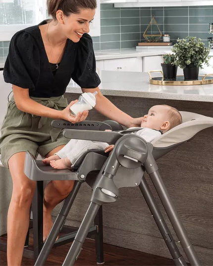 Woman feeding a baby in a high chair in a kitchen.