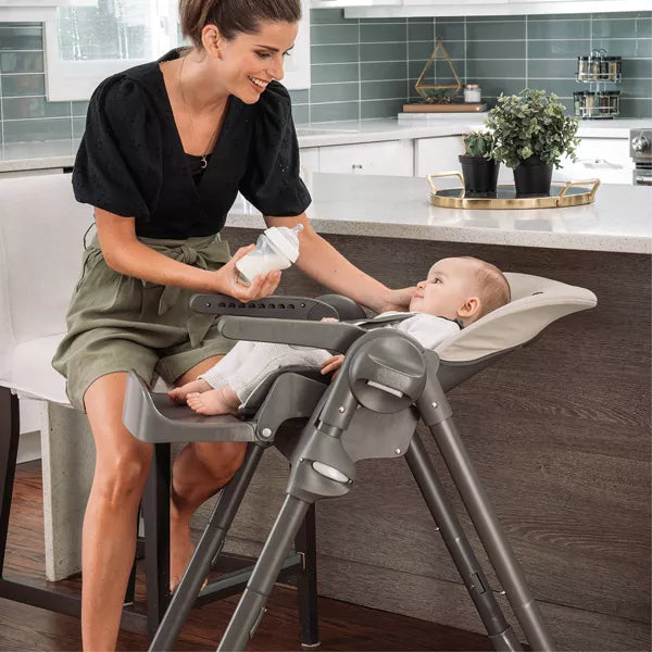 Woman feeding a baby in a high chair in a kitchen.