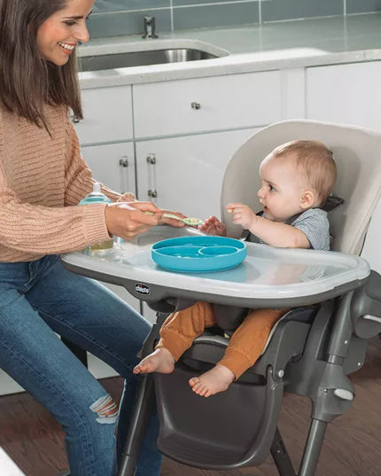 Woman feeding a baby in a high chair in a kitchen.