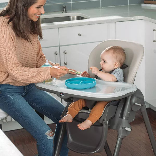 Woman feeding a baby in a high chair in a kitchen.