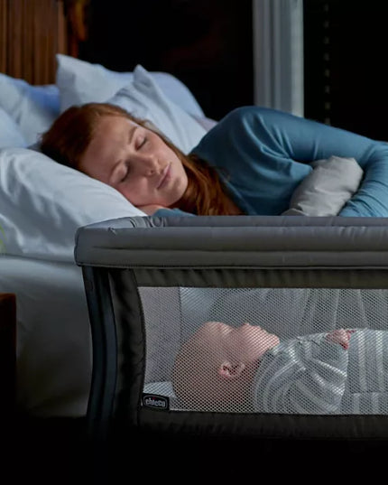 Woman sleeping in bed with a baby in a crib next to her.