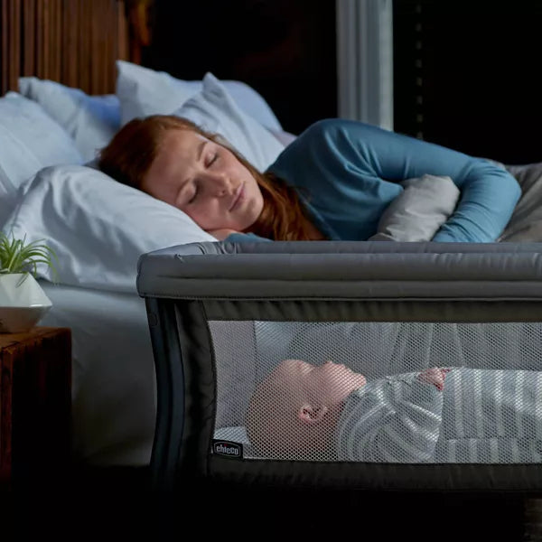 Woman sleeping in bed with a baby in a crib next to her.