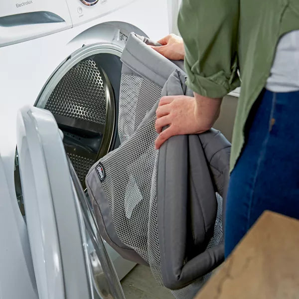 Person placing a gray mesh laundry bag into a white dryer.