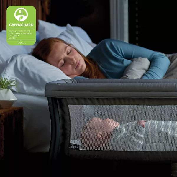 Woman lying in bed with a baby in a crib, both sleeping, with a Greenguard Gold label in the corner.