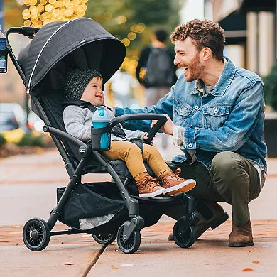 Man kneeling next to a child in a stroller on a street.
