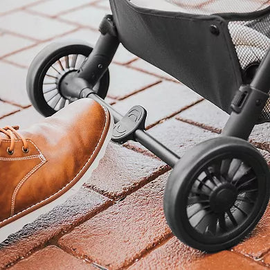 Stroller wheel on a brick pavement with a foot wearing a brown shoe stepping onto it