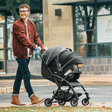 Man pushing a stroller on a sidewalk with a building in the background