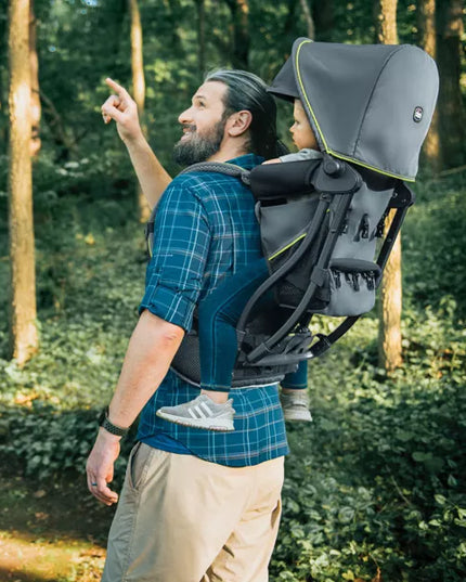 Man carrying a child in a backpack carrier through a forest